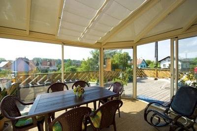 Store de toiture - modèle Oasis de marque et fabrication Reflex'Sol Véranda lumineuse avec vue sur jardin et espace repas confortable