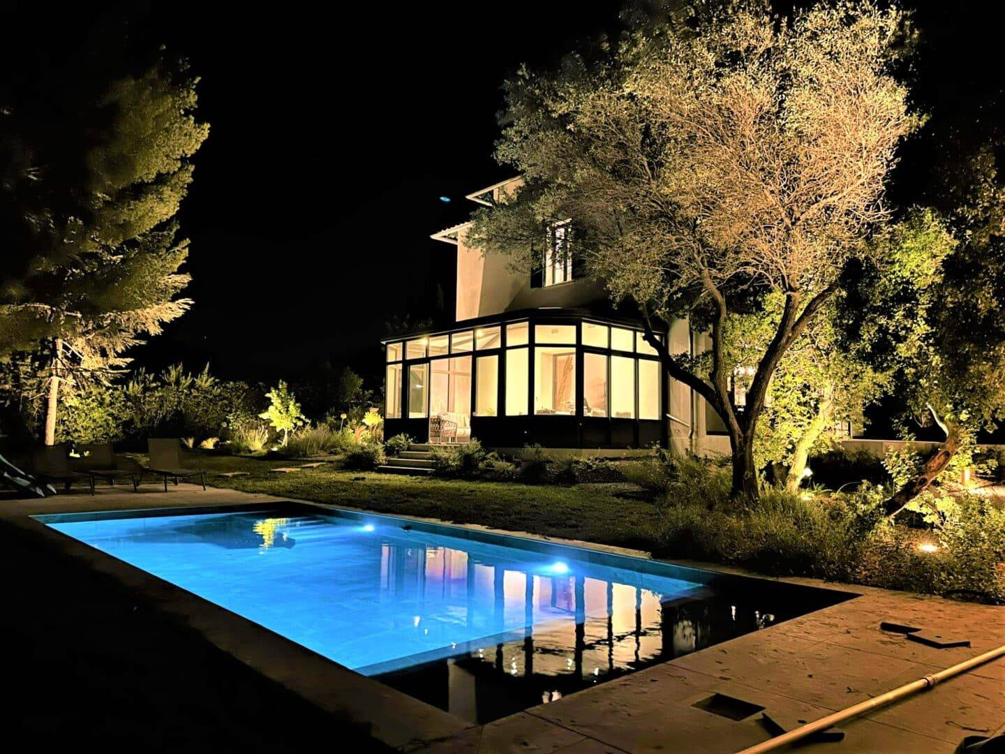 Véranda moderne éclairée la nuit près d'une piscine brillante