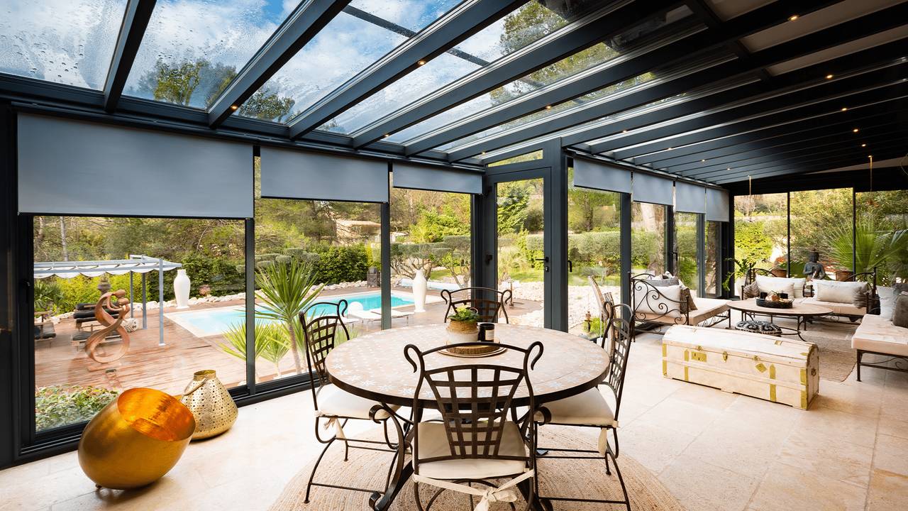 veranda-stores-toiture-stores-façade-réflexion solaire-spots-led-allège-en-muret-toiture-vitrage-interieur-vitres-stores Grand salon véranda avec stores et toit vitré