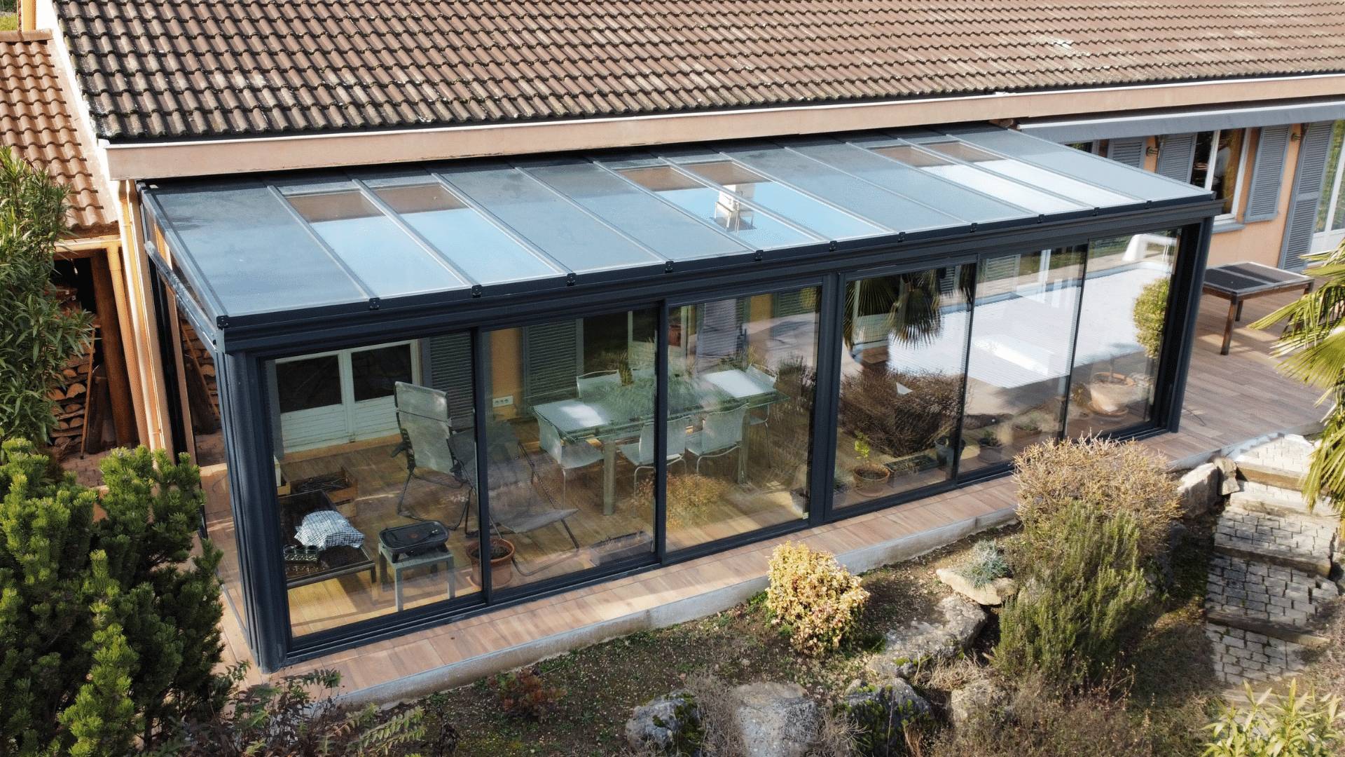 Véranda en verre moderne adossée à une maison avec jardin