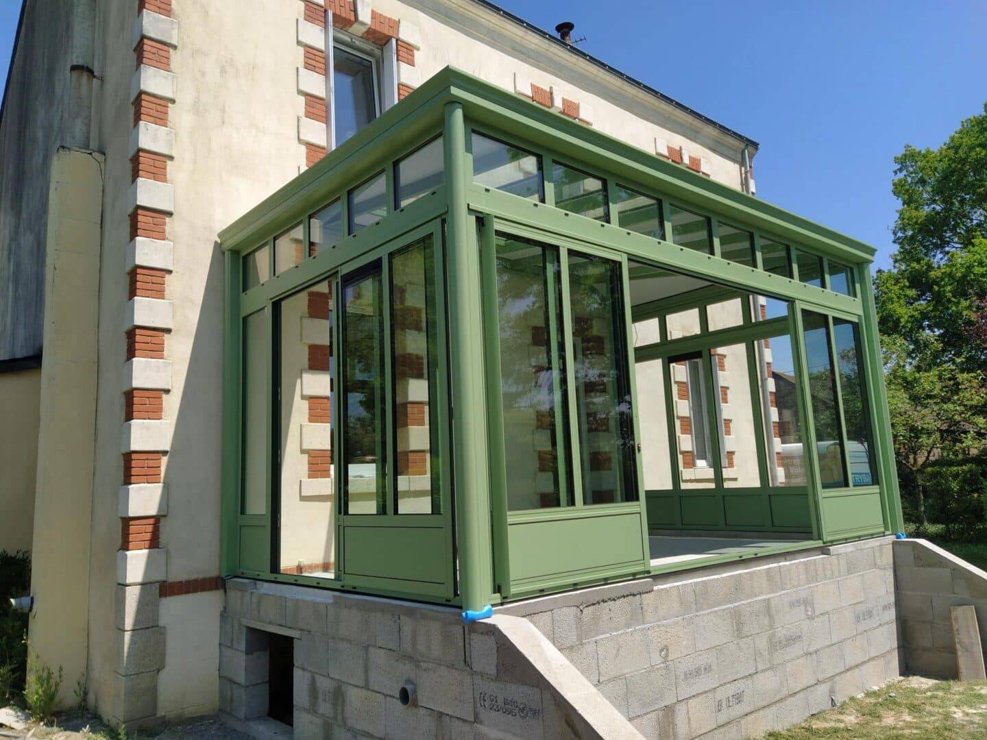 Véranda moderne verte attenante à une maison en pierre