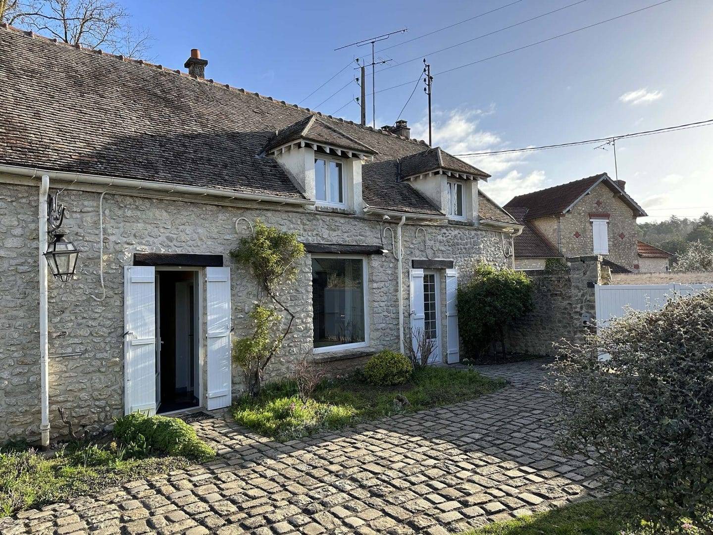 Petite véranda salon sur muret Maison en pierre avec jardin pavé et volets blancs