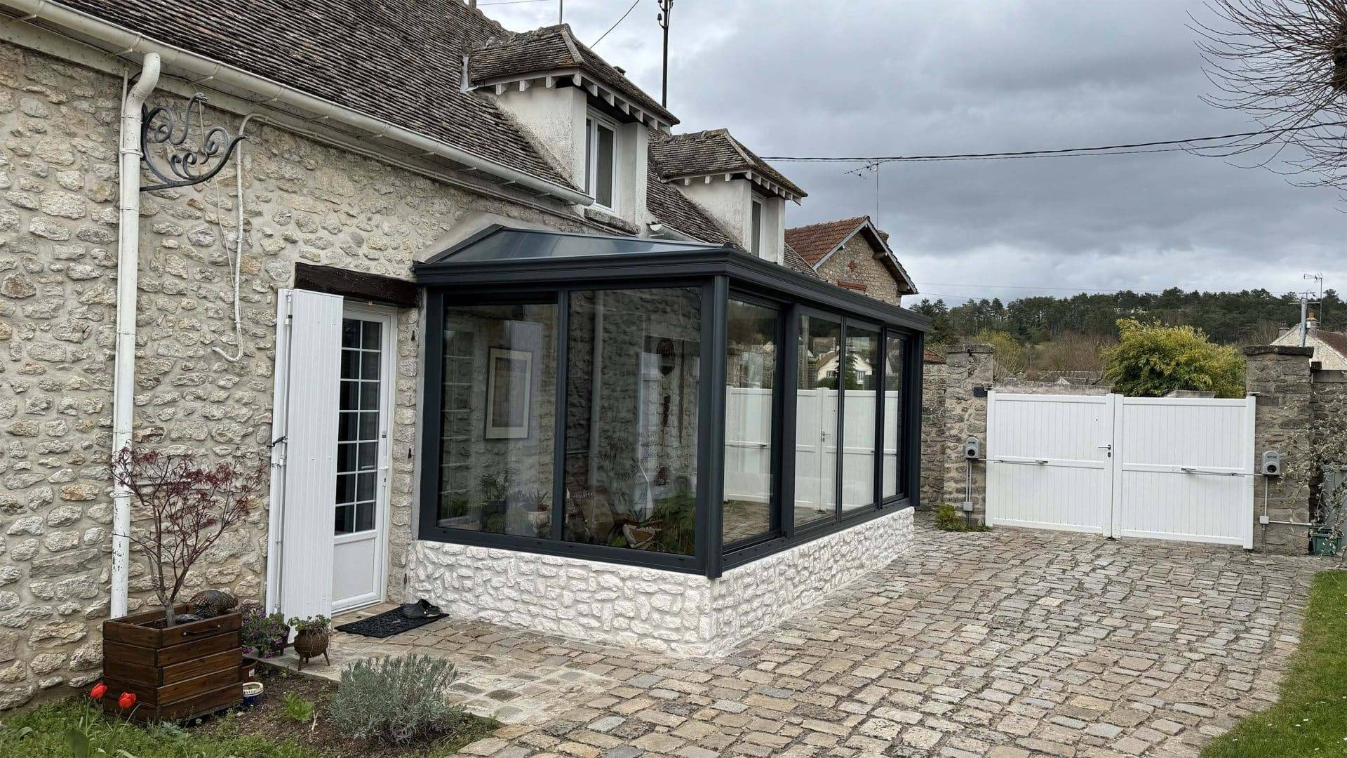 Véranda en aluminium moderne attachée à une maison en pierre