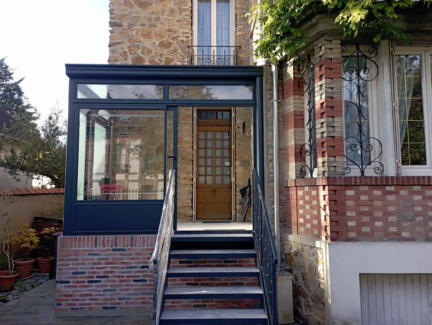 Véranda élégante en verre et métal entrée à une maison en pierre