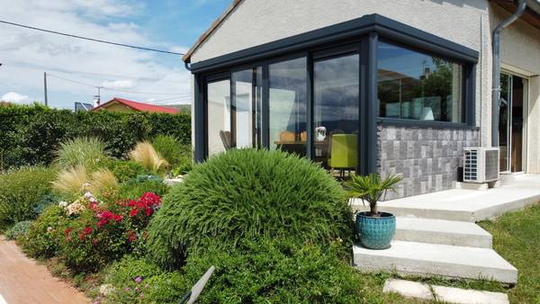 Véranda salle à manger Véranda moderne avec grandes fenêtres dans un jardin fleuri