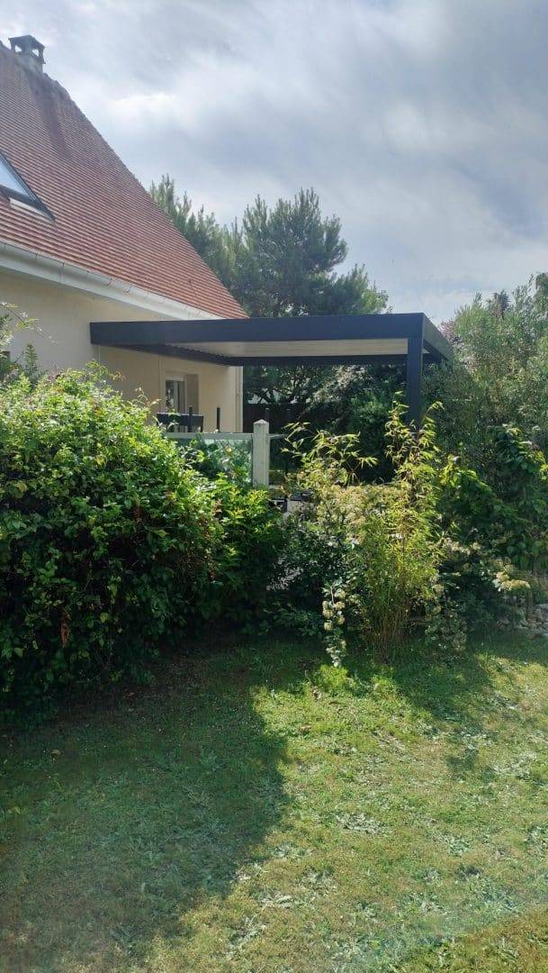 Pergola moderne attachée à une maison entourée de végétation luxuriante