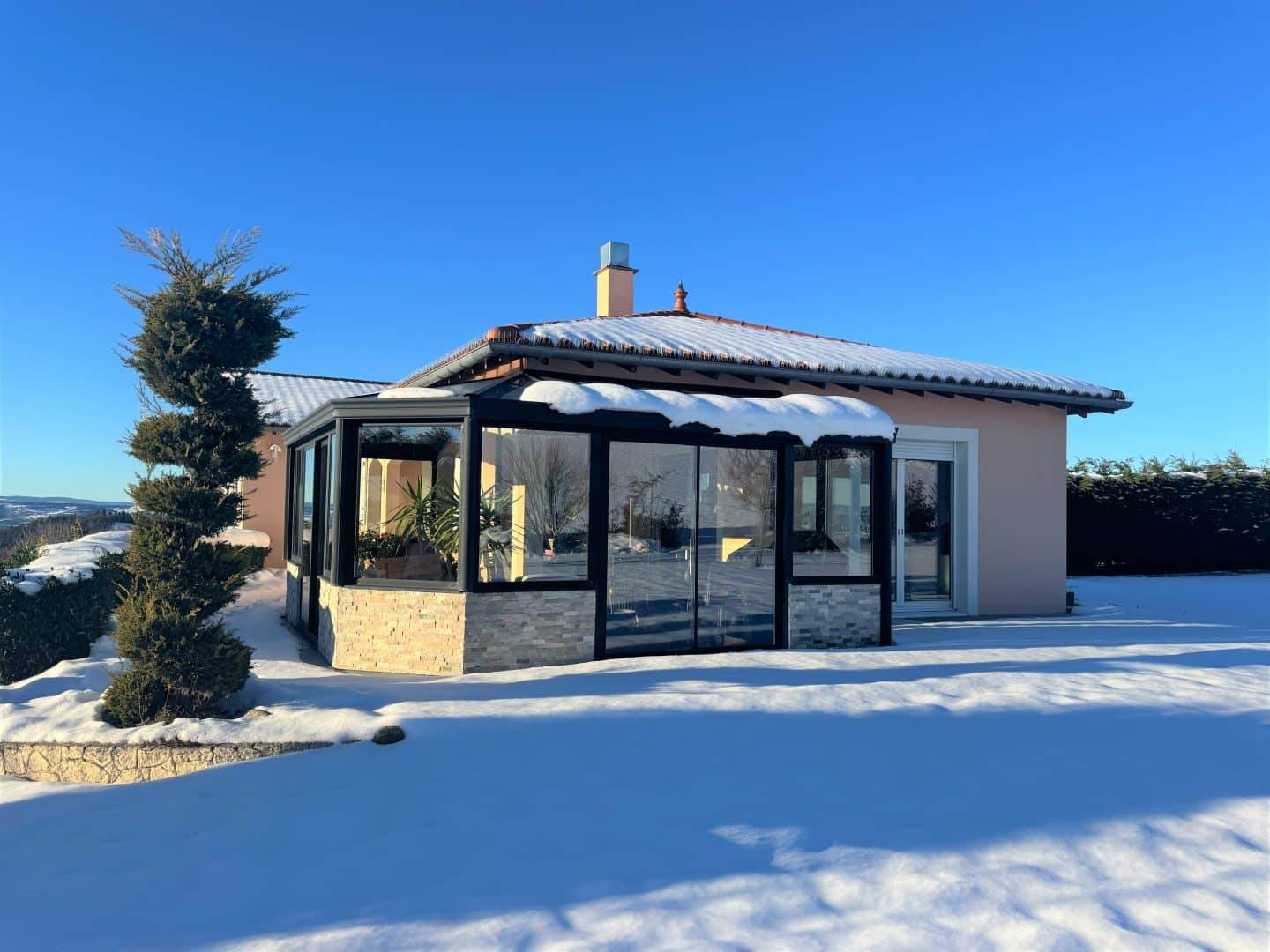 Véranda moderne en hiver entourée de neige et arbustes