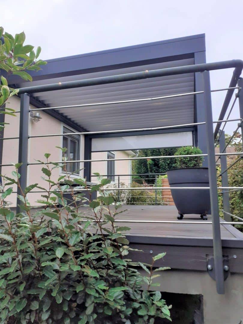 Pergola moderne en aluminium sur terrasse avec plantes vertes luxuriantes